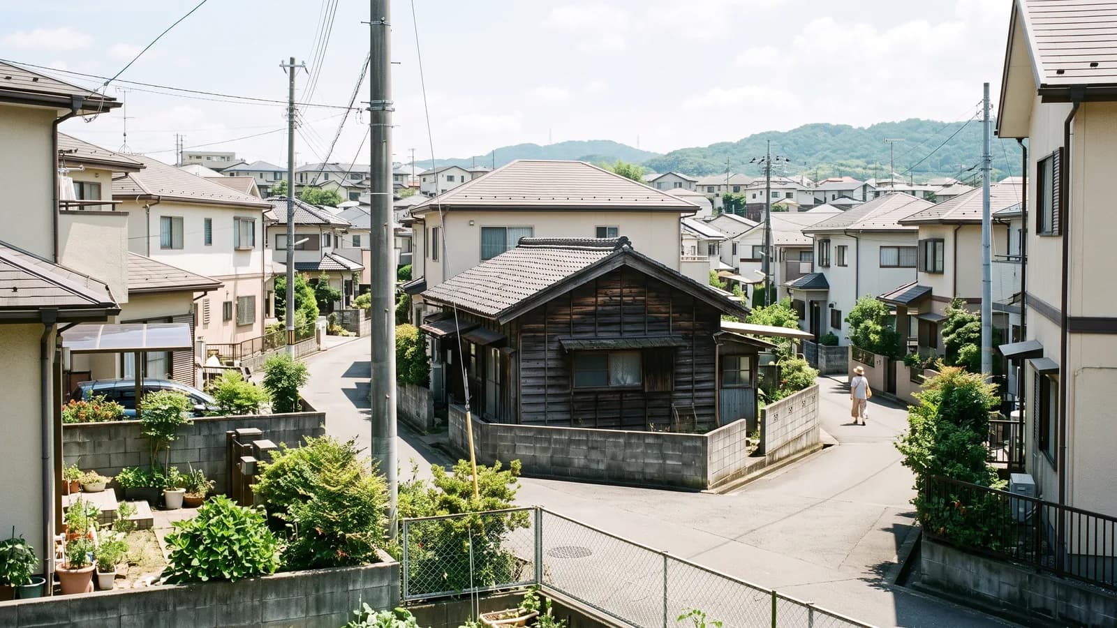 住宅街に建つ古い木造住宅と、周囲の家並みを少し離れた場所から見た様子